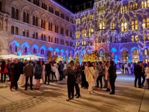 Festlich gekleidete Gäste die vor dem in Mustern angestrahlten Wiener Rathaus im Arkadenhof stehen