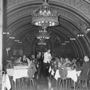 Historische schwarz-weiß Aufnahme des Rittersaals, festlich gekleidete Gäste die an weiß gedeckten Tischen sitzen und von einem Kellner in Anzug bedient werden